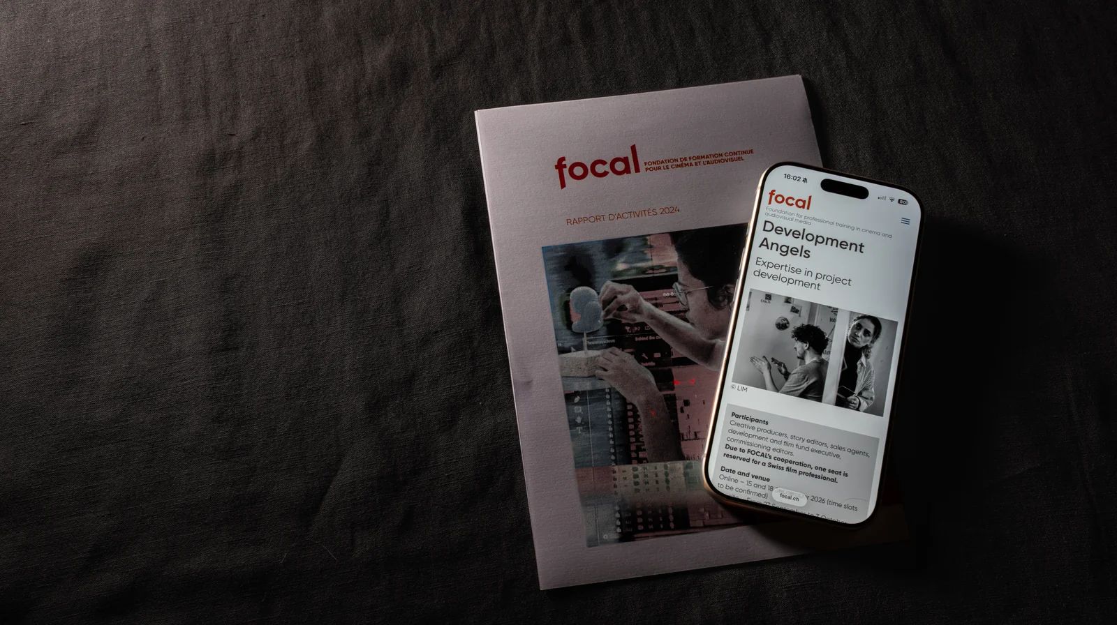 Le rapport d’activités imprimé de FOCAL, un iPhone posé dessus qui affiche une page de formation du site, dans la pénombre